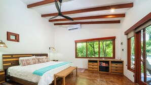 A bedroom with a bed, bedside lamps, a window with a view of greenery, a ceiling fan, and a built-in bookshelf. - Casa Amorosa: Private Villa with Pool Near Beach & Surf Break playa grande (Playa Grande)