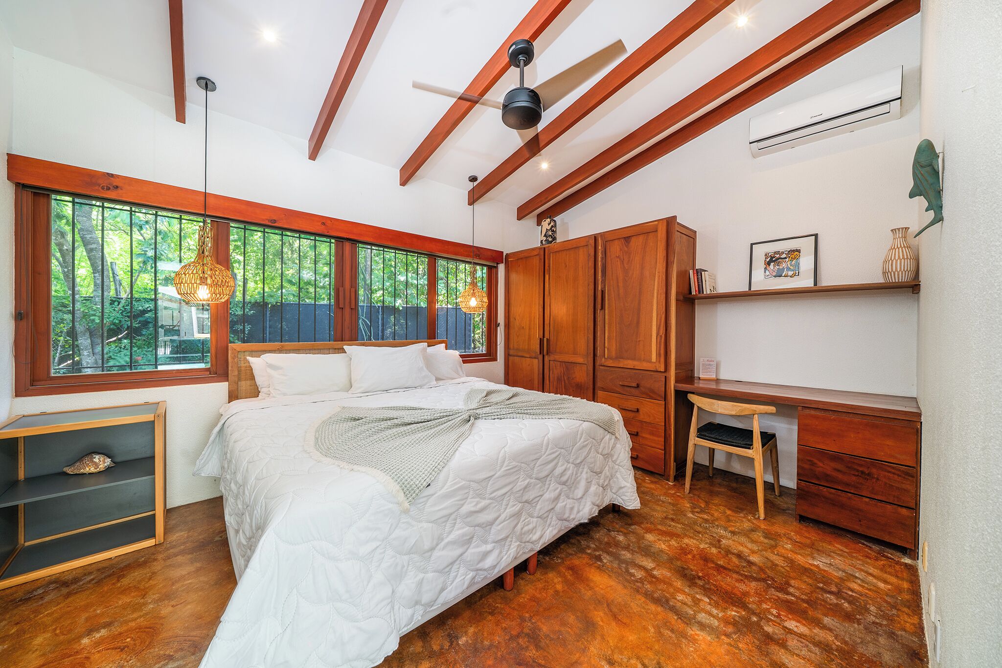 A bedroom with a bed, wooden wardrobe, desk, and shelves.