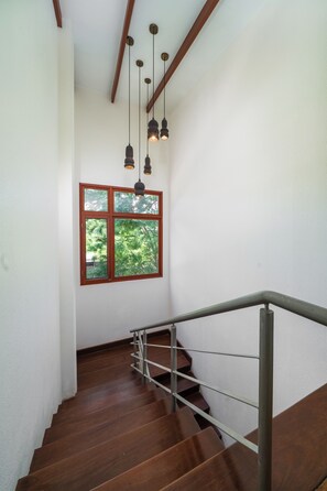 Una escalera con escalones de madera y barandillas de metal que lleva a una habitación con paredes blancas y una ventana con vistas a la vegetación.