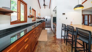 A kitchen with wooden cabinets, a stainless steel refrigerator, and a dining area with a table and chairs. - Casa Amorosa: Private Villa with Pool Near Beach & Surf Break playa grande (Playa Grande)