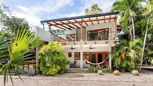 A modern two-story house with a covered patio, surrounded by tropical vegetation. - Casa Amorosa: Private Villa with Pool Near Beach & Surf Break playa grande (Playa Grande)