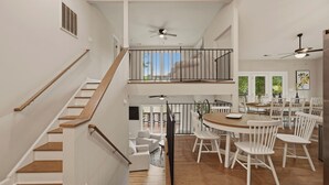 A spacious interior with a staircase, a dining area with white chairs, and a balcony with a view. - Poolside Paradise by Avantstay Waterfront Home + Pool + Spa Dock + Game Room Near Hiking (Sherrills Ford)