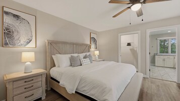 Un dormitorio con cama, mesitas de noche, ventilador de techo y obras de arte en las paredes.