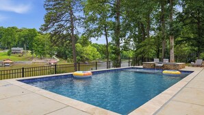 A rectangular swimming pool with two inflatable rings, surrounded by a stone deck and a black metal fence. - Poolside Paradise by Avantstay Waterfront Home + Pool + Spa Dock + Game Room Near Hiking (Sherrills Ford)