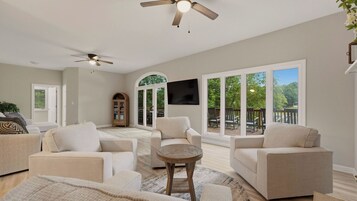 Amplia sala de estar con ventilador de techo, televisor y vistas al exterior.
