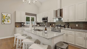 Una cocina moderna con armarios blancos, encimeras de granito, electrodomésticos de acero inoxidable y una isla grande con taburetes de bar.