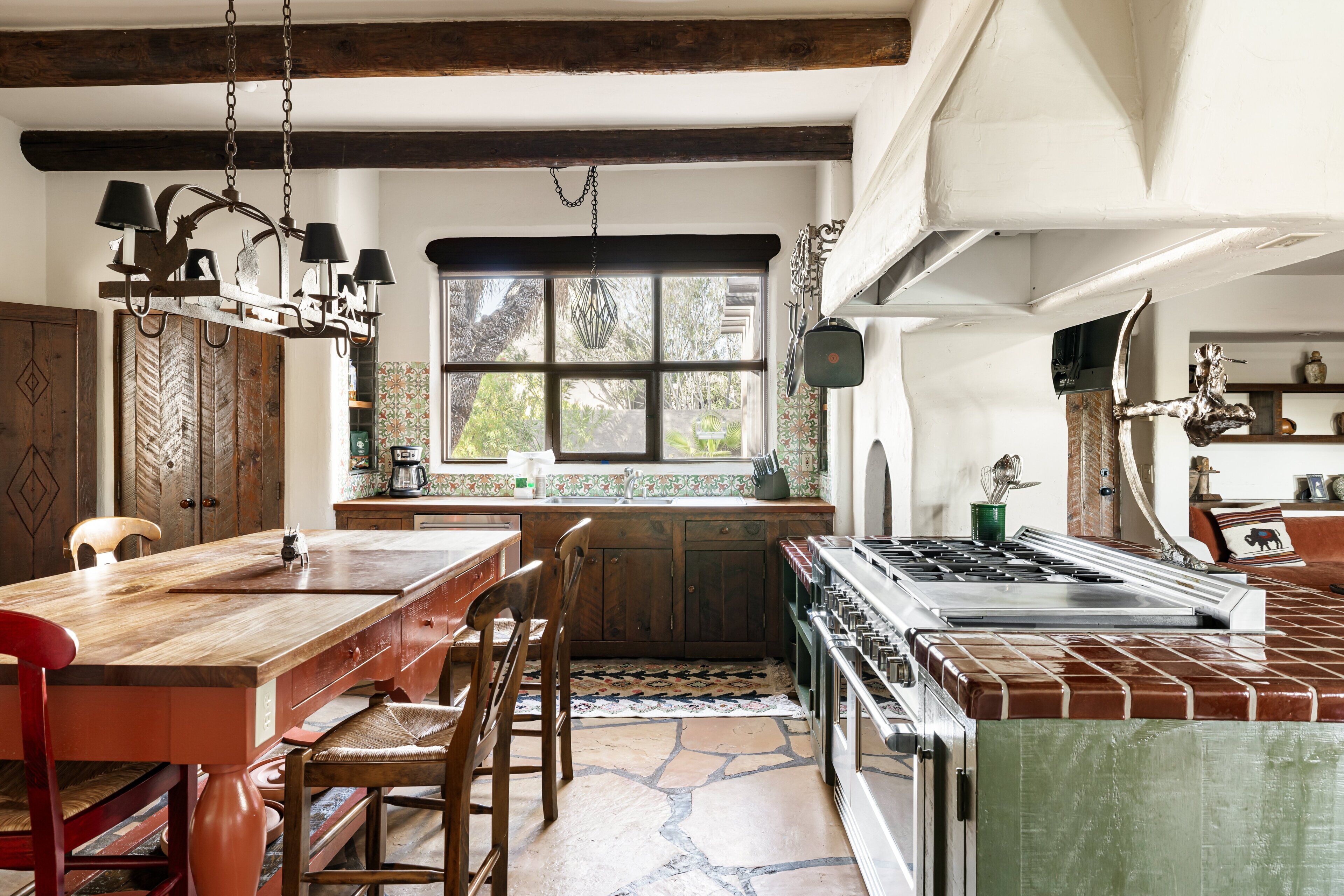 Une cuisine rustique dotée d’un grand îlot central, de meubles en bois, d’une cuisinière et d’une fenêtre offrant une belle vue.
