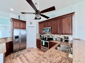 A kitchen with wooden cabinets, stainless steel appliances, a ceiling fan, and a patterned rug. - Sandy Beach Retreat and Gulf View (Galveston)