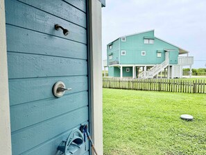 A teal building with a wooden fence, a grassy yard, and a small round object on the ground. - Sandy Beach Retreat and Gulf View (Galveston)