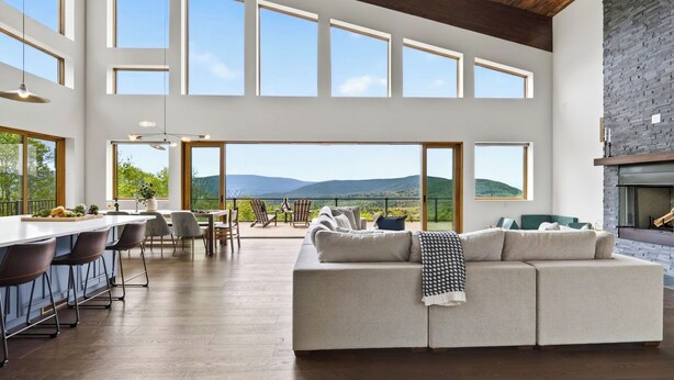 A spacious living area with a large sofa, dining table, and chairs, large windows offering a view of the outdoors. - Bates Ridge by Avantstay Secluded Catskills Retreat Near Hunter Mountain + Game Room (Haines Falls)