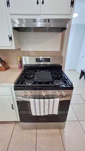 A kitchen with a stainless steel stove, a range hood, and a white cabinet with black handles.