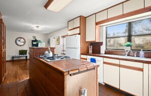 A kitchen with a central island, wooden cabinets, a refrigerator, and a window with a view. - Peaceful 4-bedroom house with AC in Baton Rouge (Baton Rouge)