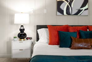A neatly made bed with white and teal bedding, a black lamp on a white nightstand, and a large abstract painting on the wall. - Peaceful 4-bedroom house with AC in Baton Rouge (Baton Rouge)
