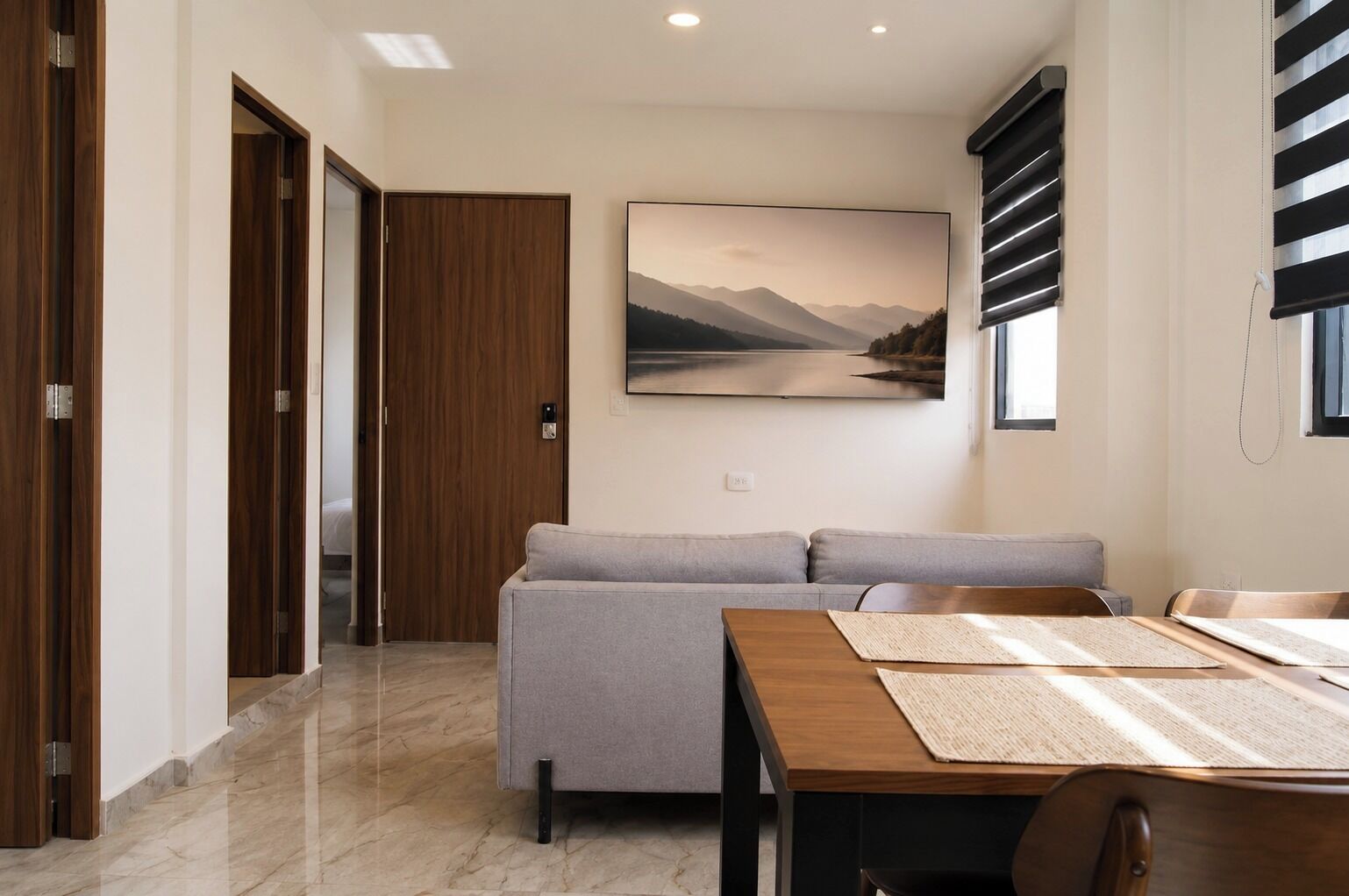 A modern living room with a sofa, a dining table, and a painting of a landscape.