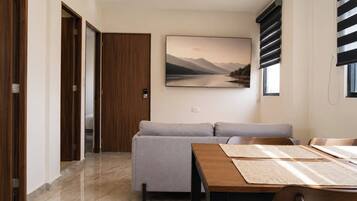 A modern living room with a sofa, a dining table, and a painting of a landscape.