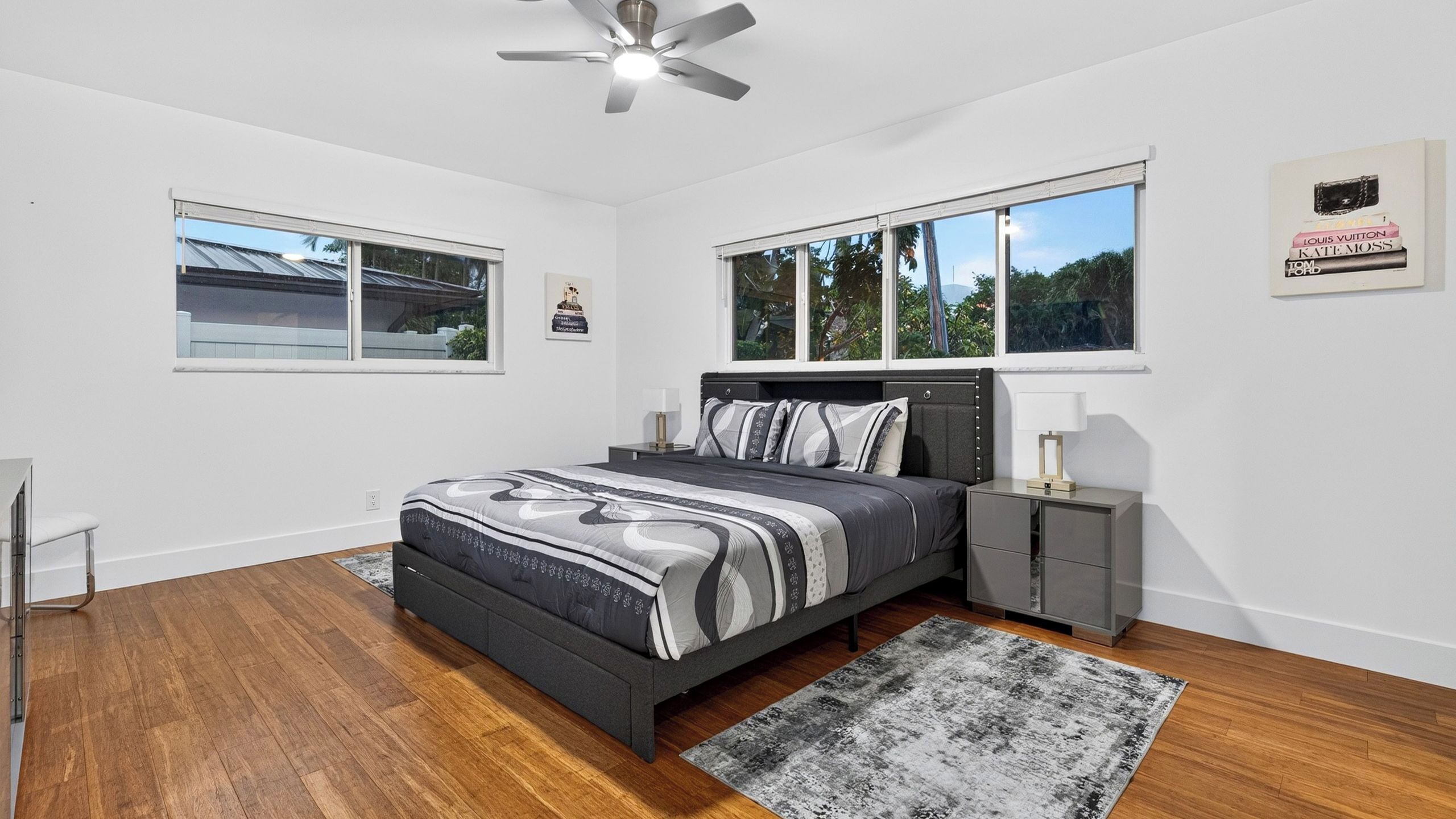 A bedroom with a bed, bedside tables, a ceiling fan, and large windows.