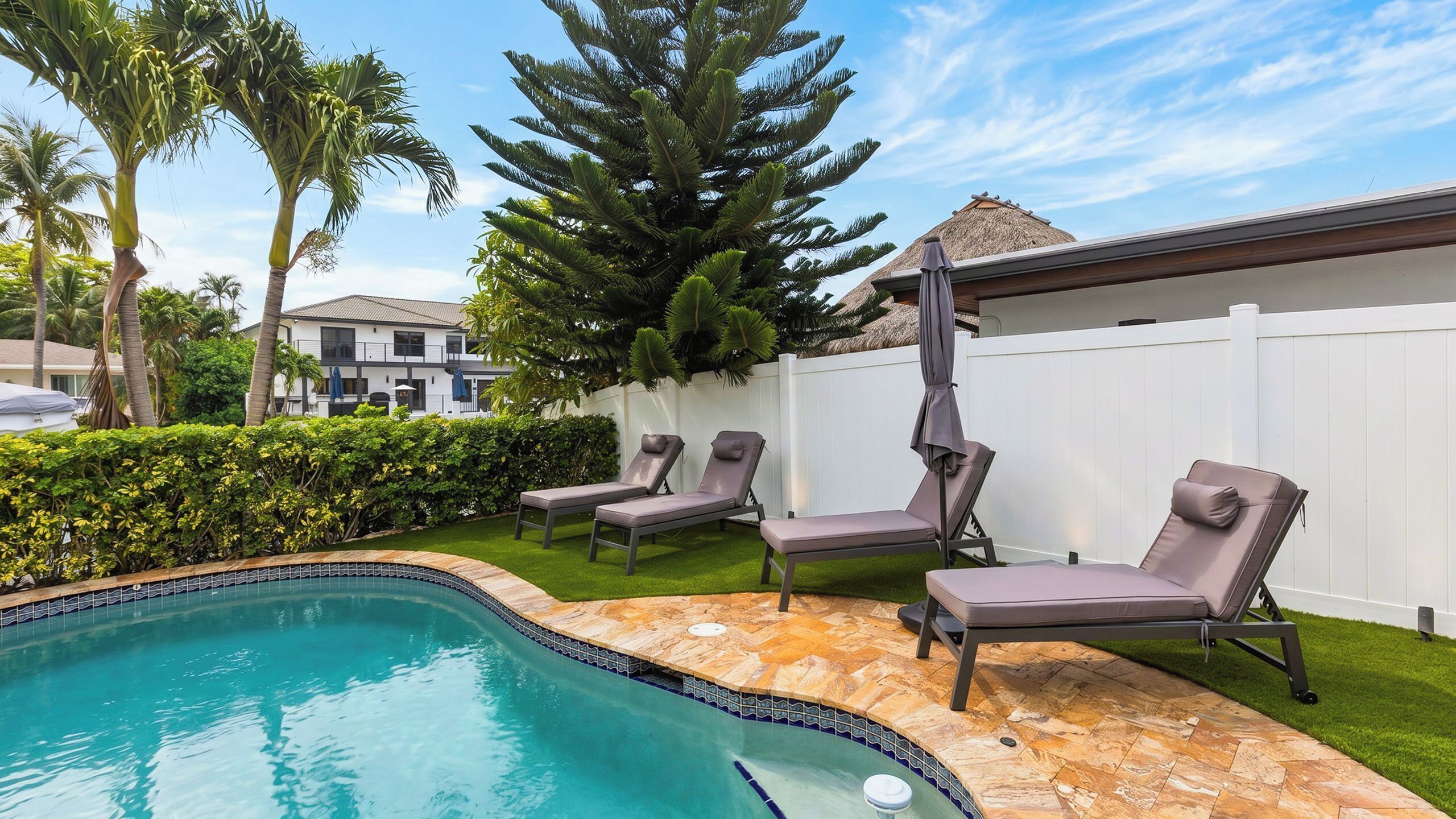 A swimming pool with lounge chairs and a white fence.