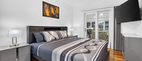 Une chambre moderne avec un lit, des tables de chevet, un ventilateur de plafond, un tableau et une vue à travers une porte vitrée.