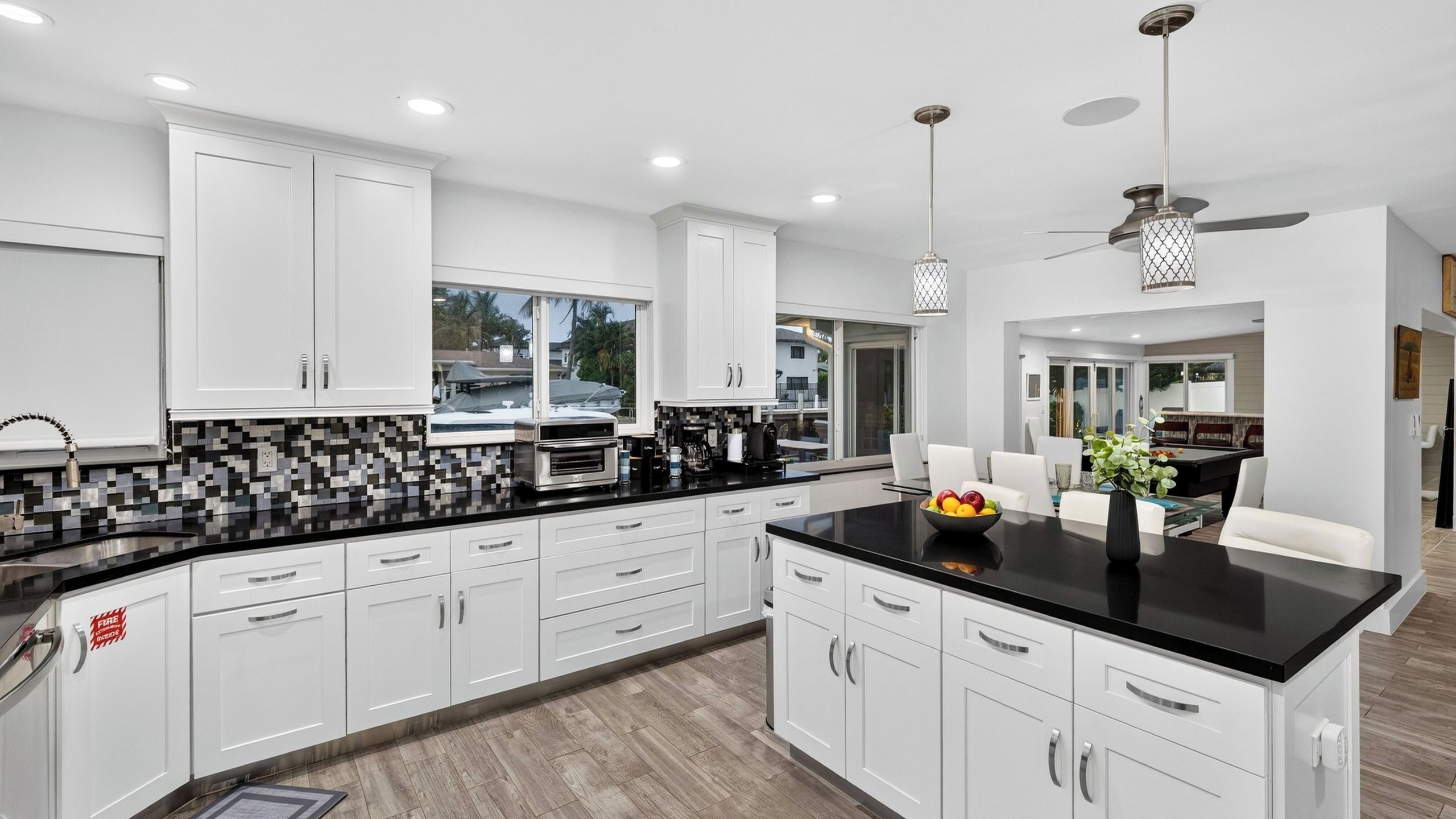 A modern kitchen with white cabinets, a black countertop, and a central island with fruit.