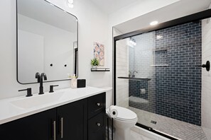 Ein modernes Badezimmer mit einem weißen Waschbecken, schwarzen Schränken, einem großen Spiegel und einer Duschkabine aus Glas.
