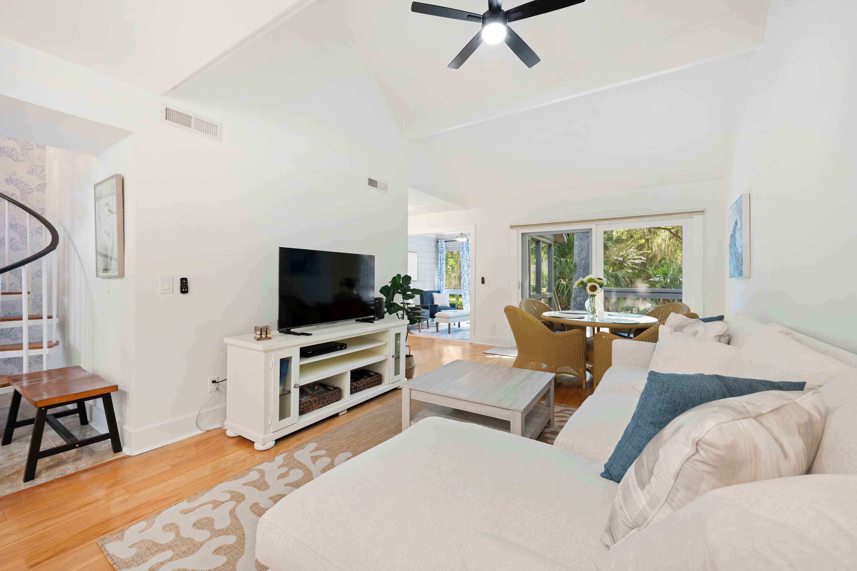 A modern living room with a flat-screen TV, a white sofa, a coffee table, and a dining area with a table and chairs.