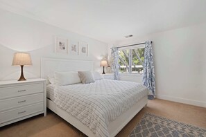 Ein Schlafzimmer mit Bett, Nachttischen, einer Lampe, einem Fenster mit Vorhängen und Wandbildern.