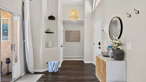 A hallway with a wooden floor, a hanging light fixture, a mirror, and a door with a white frame. - The Light of the Desert by Avantstay Pool + Firepit + BBQ Mins to National Park + DT Yucca Valley (Yucca Valley)