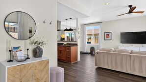 A modern living room with a sofa, a TV, and a kitchen area with wooden cabinets and a dining table. - The Light of the Desert by Avantstay Pool + Firepit + BBQ Mins to National Park + DT Yucca Valley (Yucca Valley)