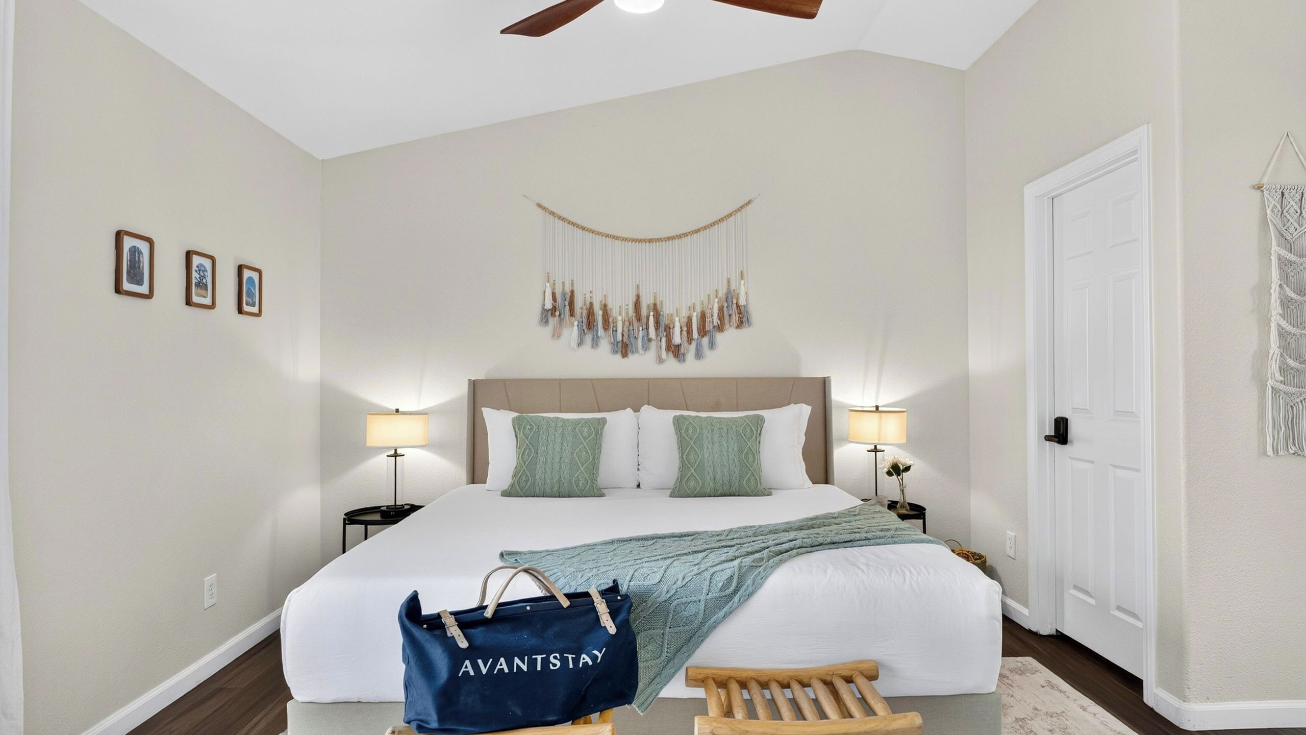 A bedroom with a bed, two bedside tables with lamps, a macrame wall hanging, and a door.