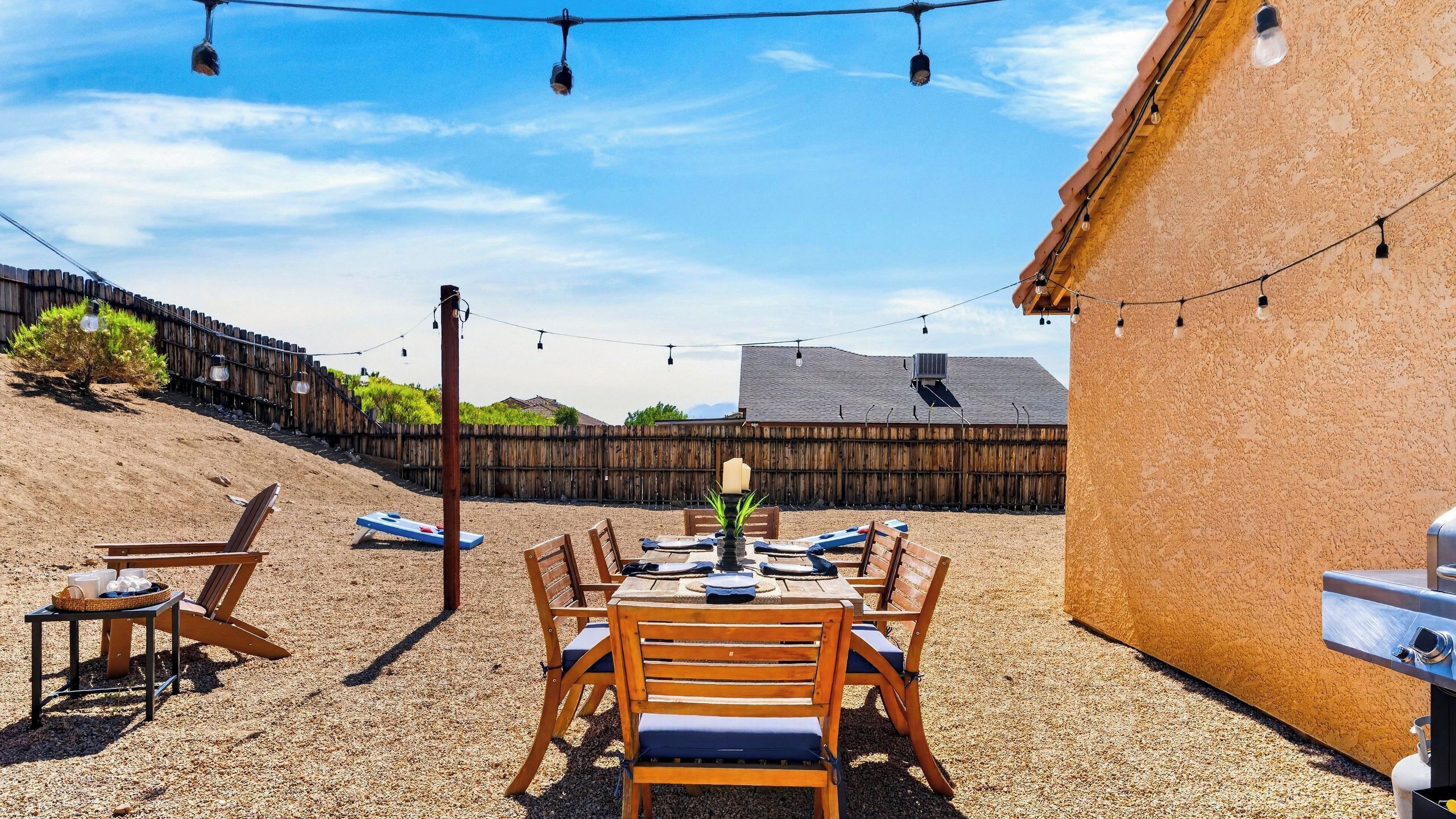 An outdoor patio with a table and chairs, string lights, and a barbecue grill.