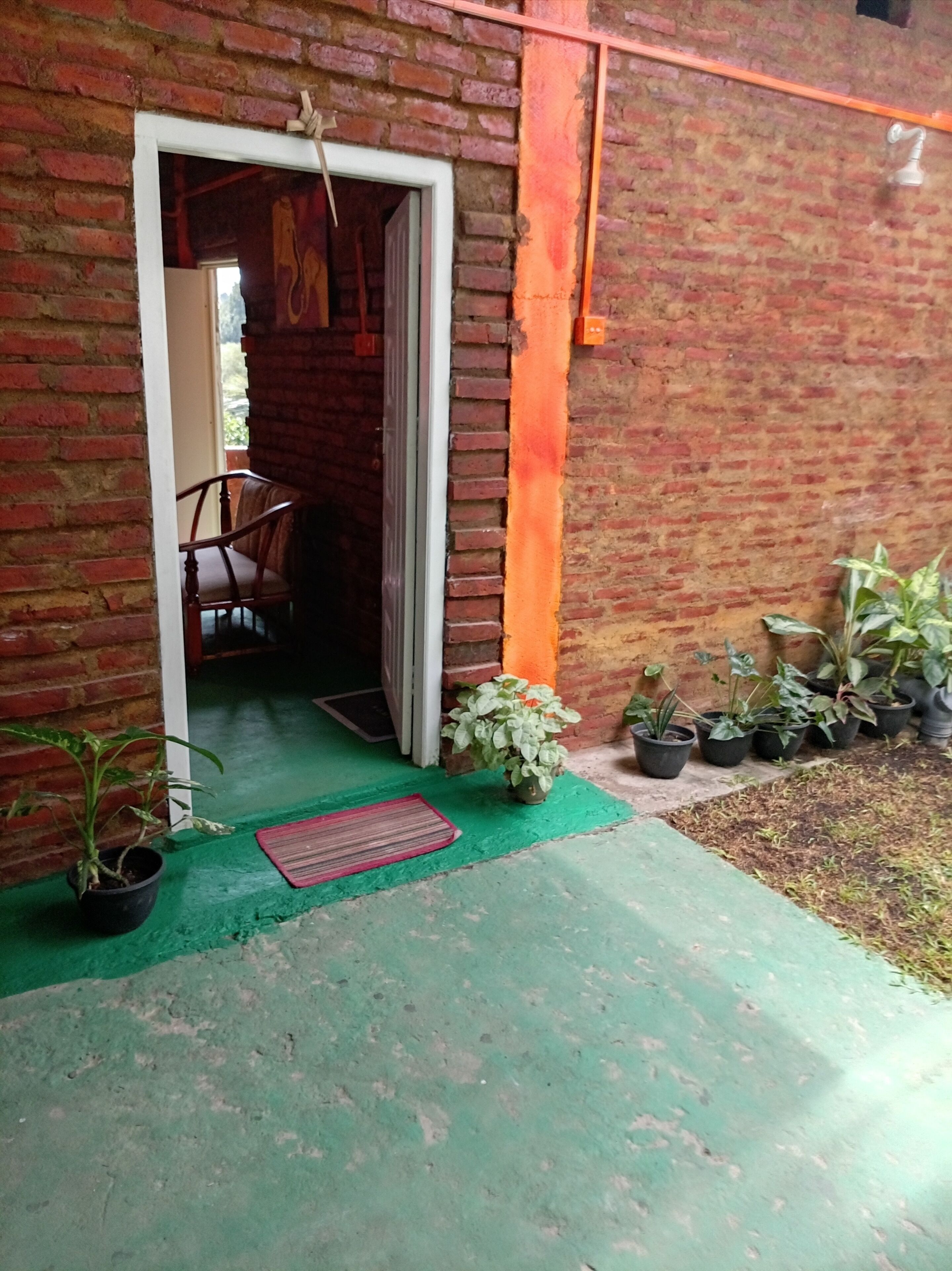 A brick building with a doorway leading to an interior space, a green mat at the entrance, and potted plants outside.