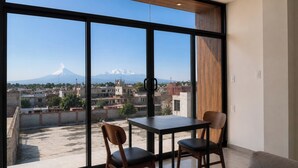 Una habitación con ventanas amplias, una mesa, dos sillas y vistas a una montaña.