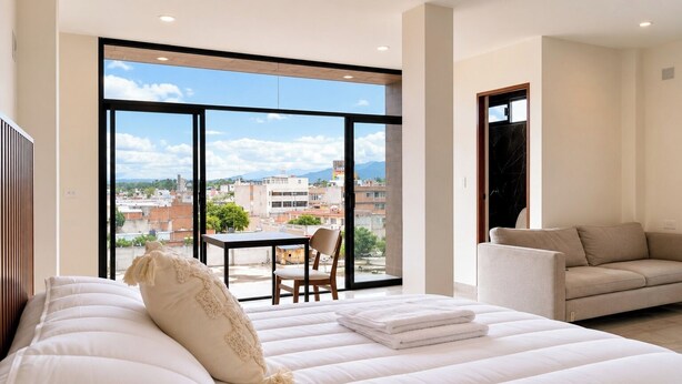 Un dormitorio con una cama grande, un sofá, una mesa de comedor y vistas a la ciudad.