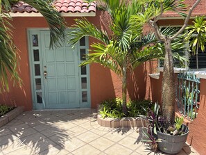 A building with a blue door, a tiled patio, and various plants. - Charming studio apartment, centrally located with a garden. (Cozumel)