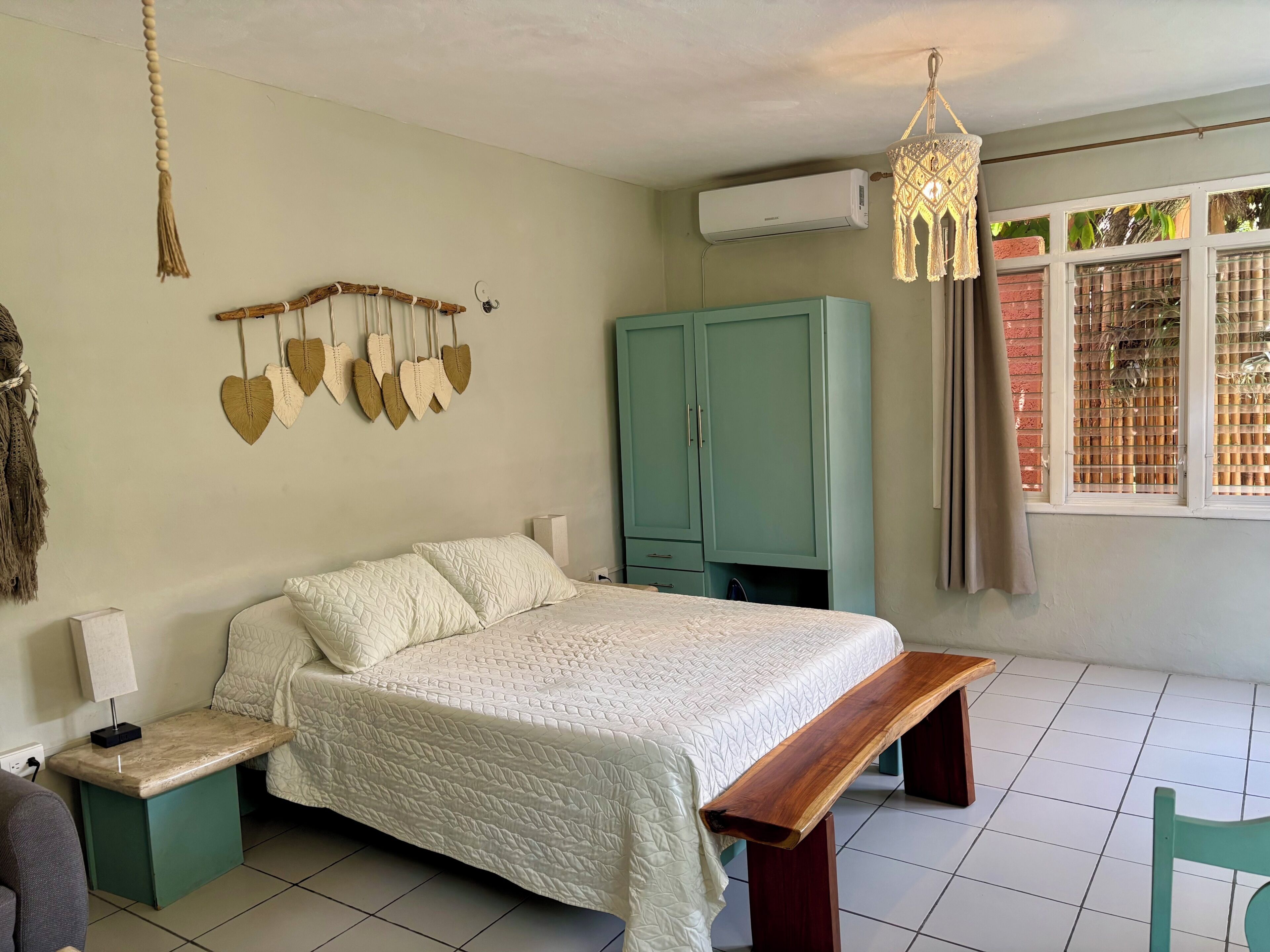 Een slaapkamer met een bed, nachtkastjes, een houten bankje, een hanglamp en een kledingkast.