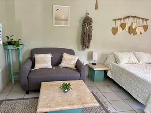 A room with a sofa, a bed, a small table with a plant, a wall-mounted light, and a wall decoration. - Charming studio apartment, centrally located with a garden. (Cozumel)