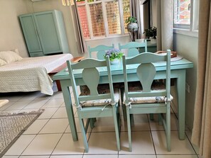 Une pièce comprenant un lit, une table à manger avec des chaises, un meuble et une fenêtre donnant sur un immeuble.