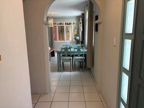 A hallway leading to a dining area with a table and chairs, a hanging light fixture, and a window with curtains. - Charming studio apartment, centrally located with a garden. (Cozumel)