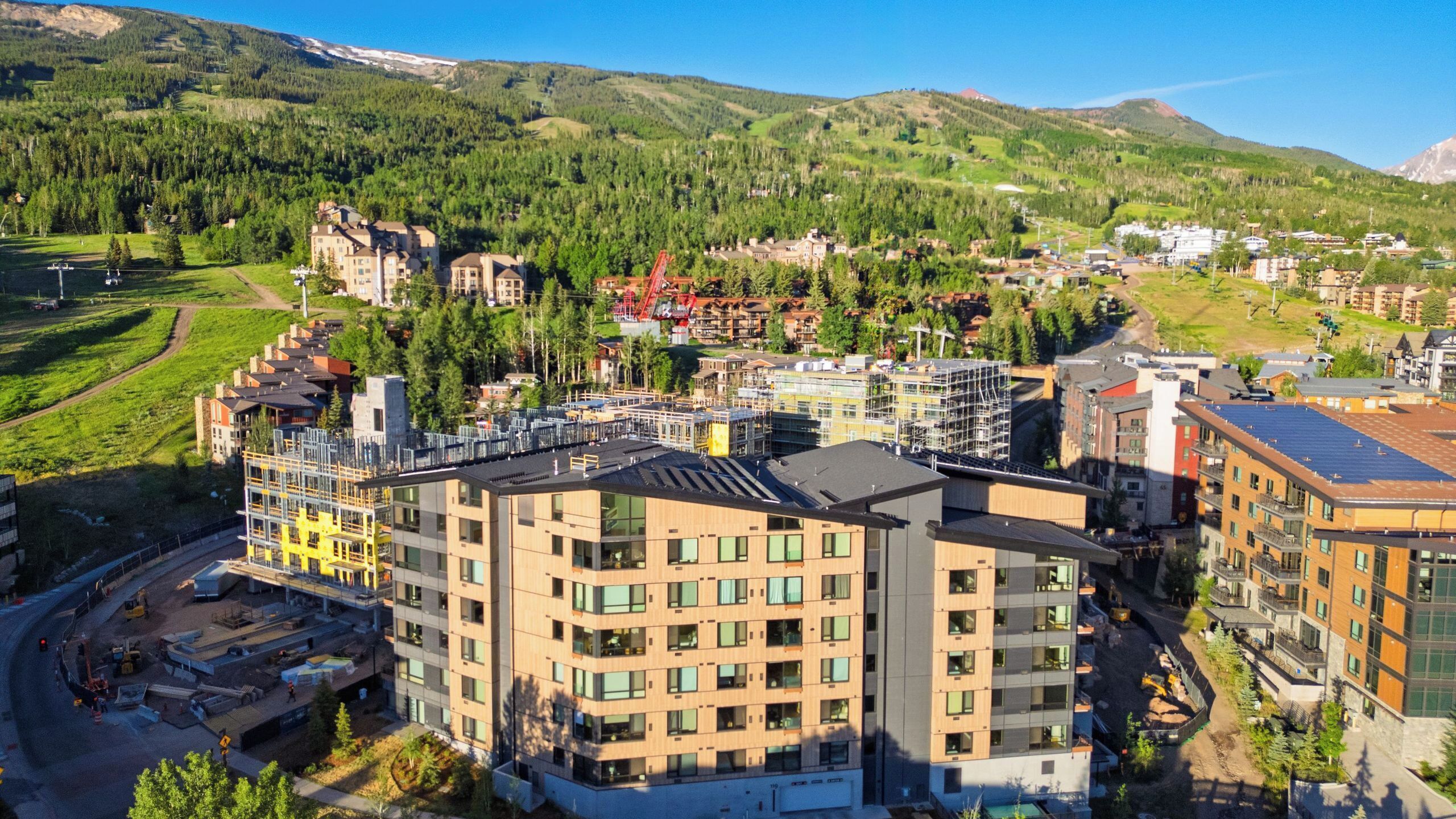 A modern hotel with multiple floors, a parking area, and a view of surrounding hills and trees.