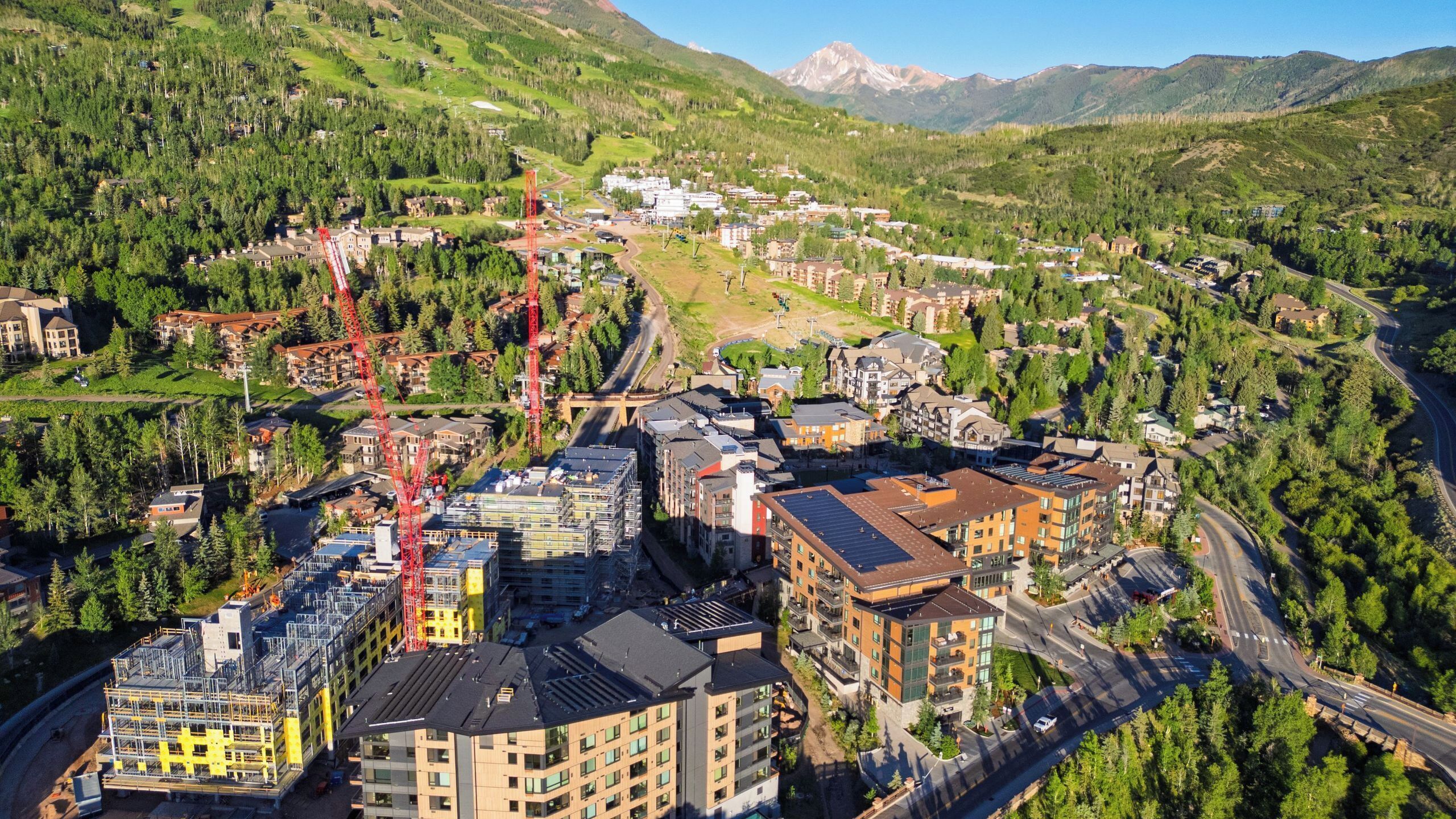 A mountainous town with modern buildings, roads, and a prominent red crane.