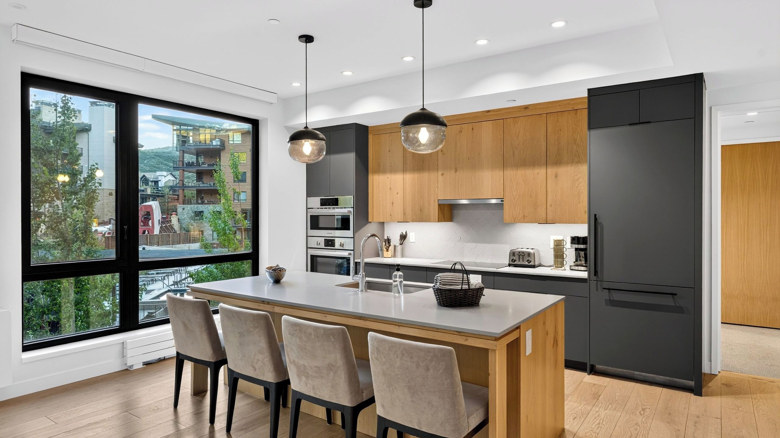 Een moderne keuken met een groot eiland, houten kastjes en uitzicht op een woonwijk.