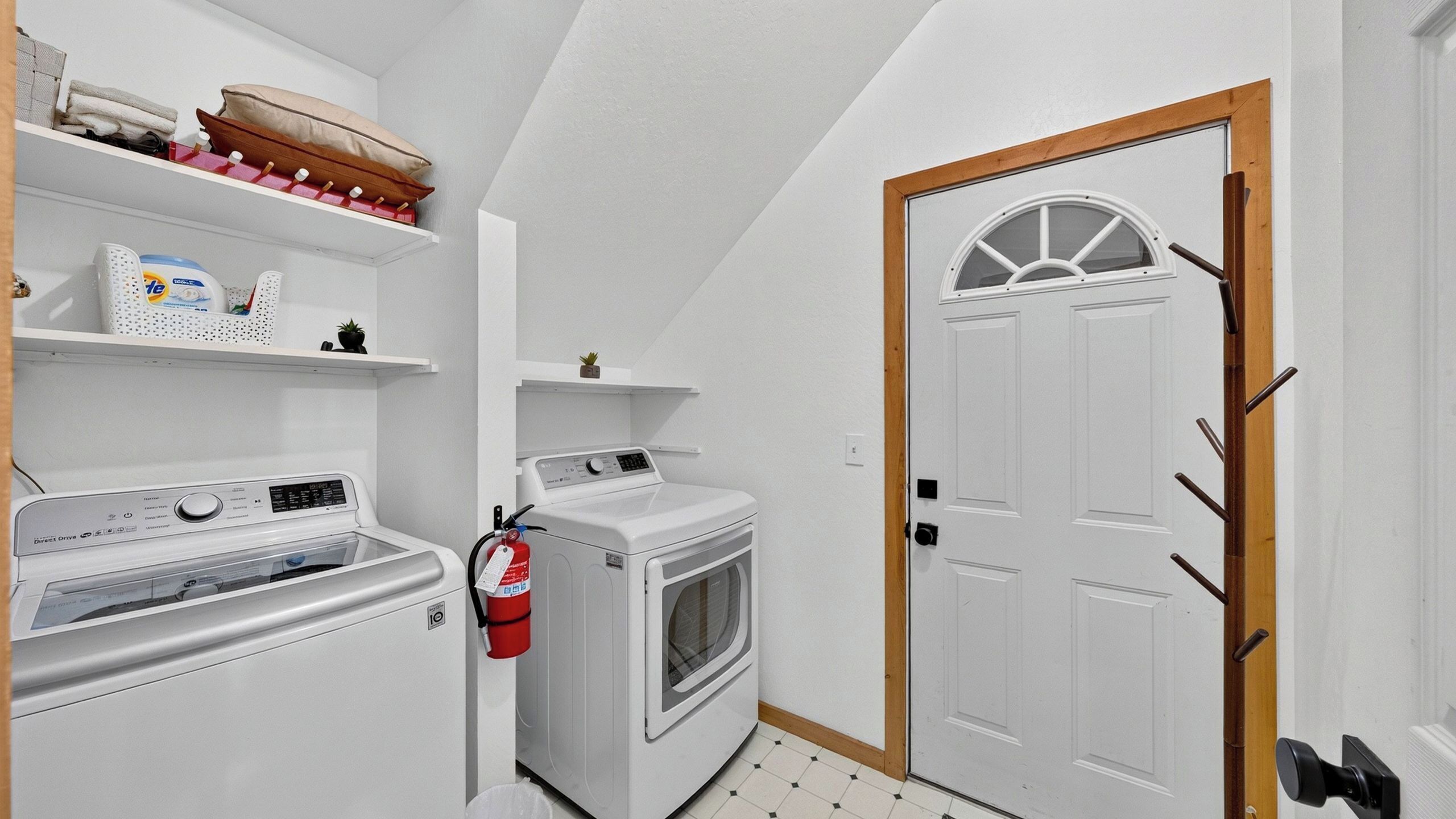 A laundry room with a washing machine, dryer, and shelves with laundry supplies.