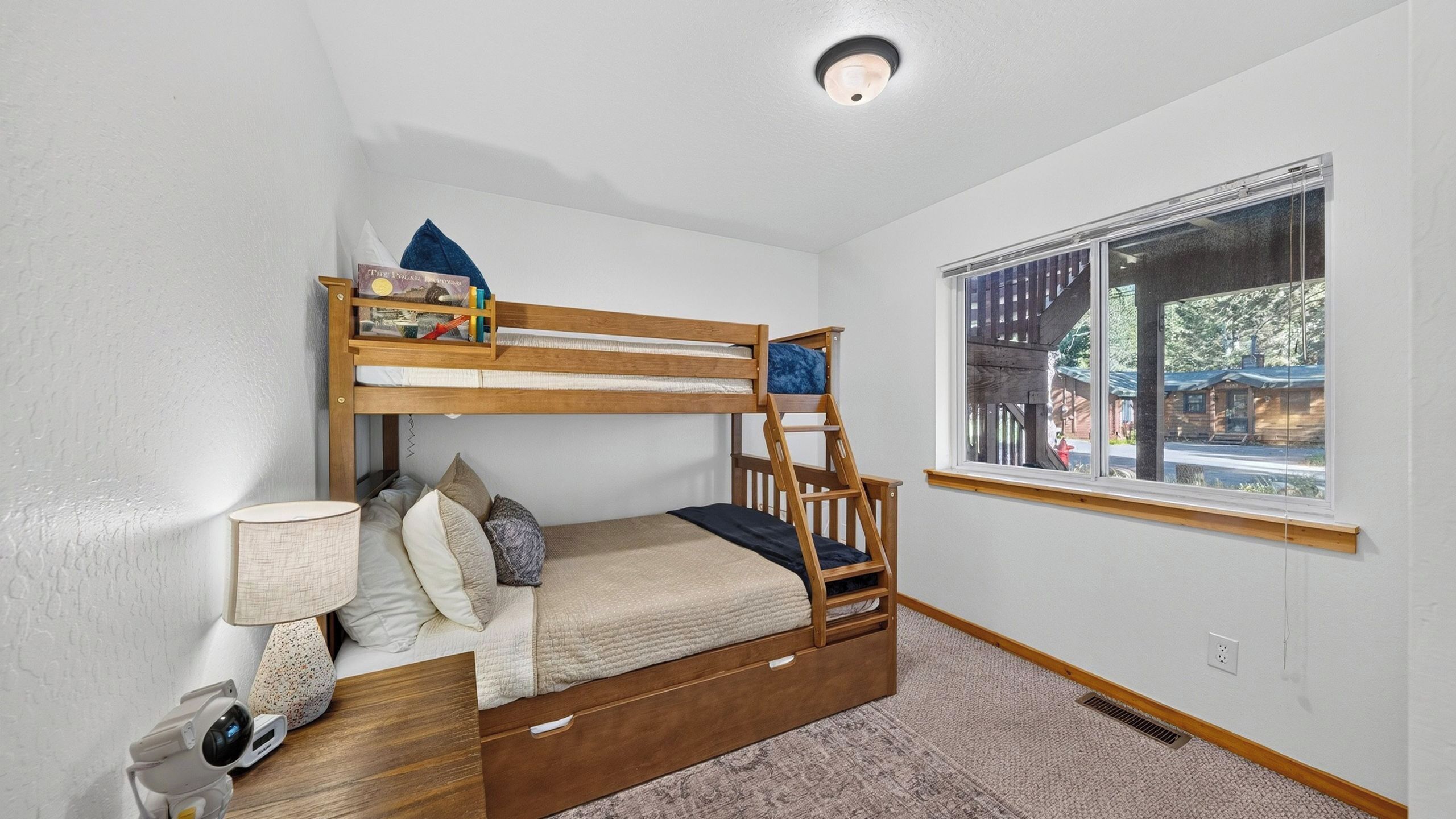 Dormitorio con literas, ventana, lámpara y una mesita.