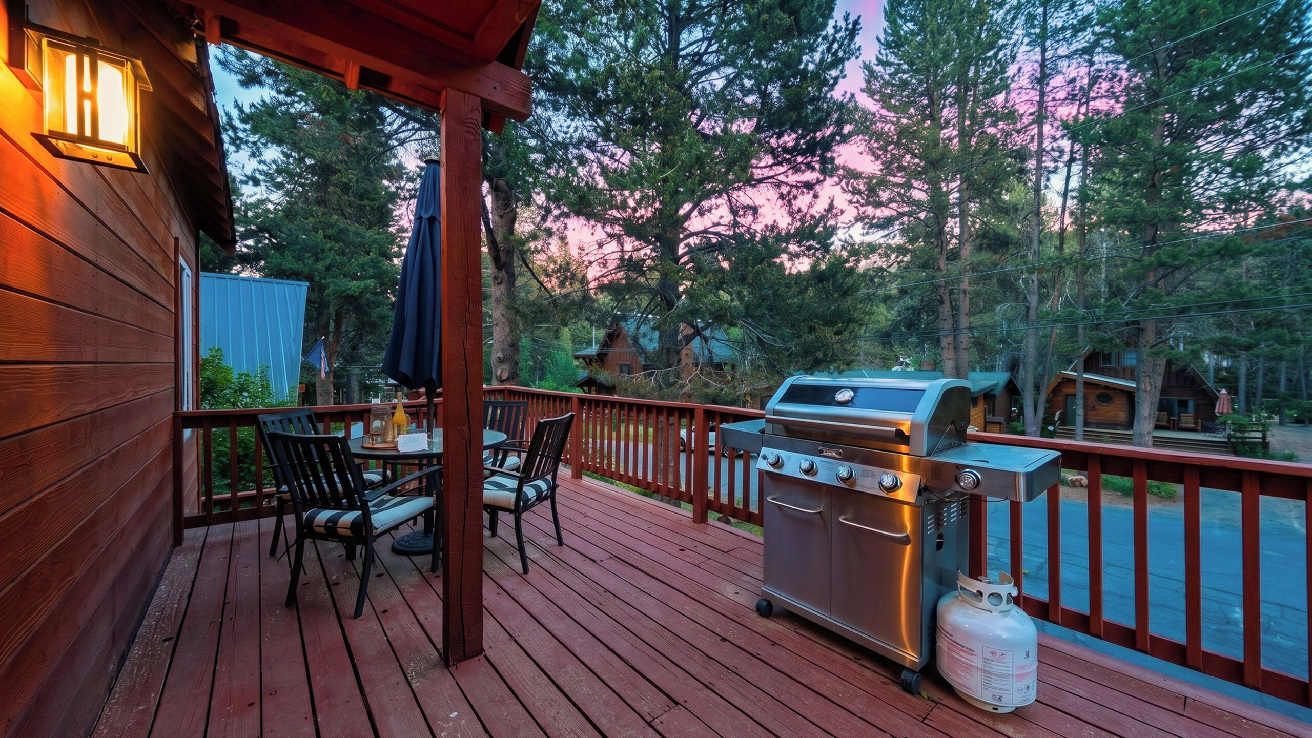 Una terraza de madera con una parrilla y sillas, con vista a un área boscosa.