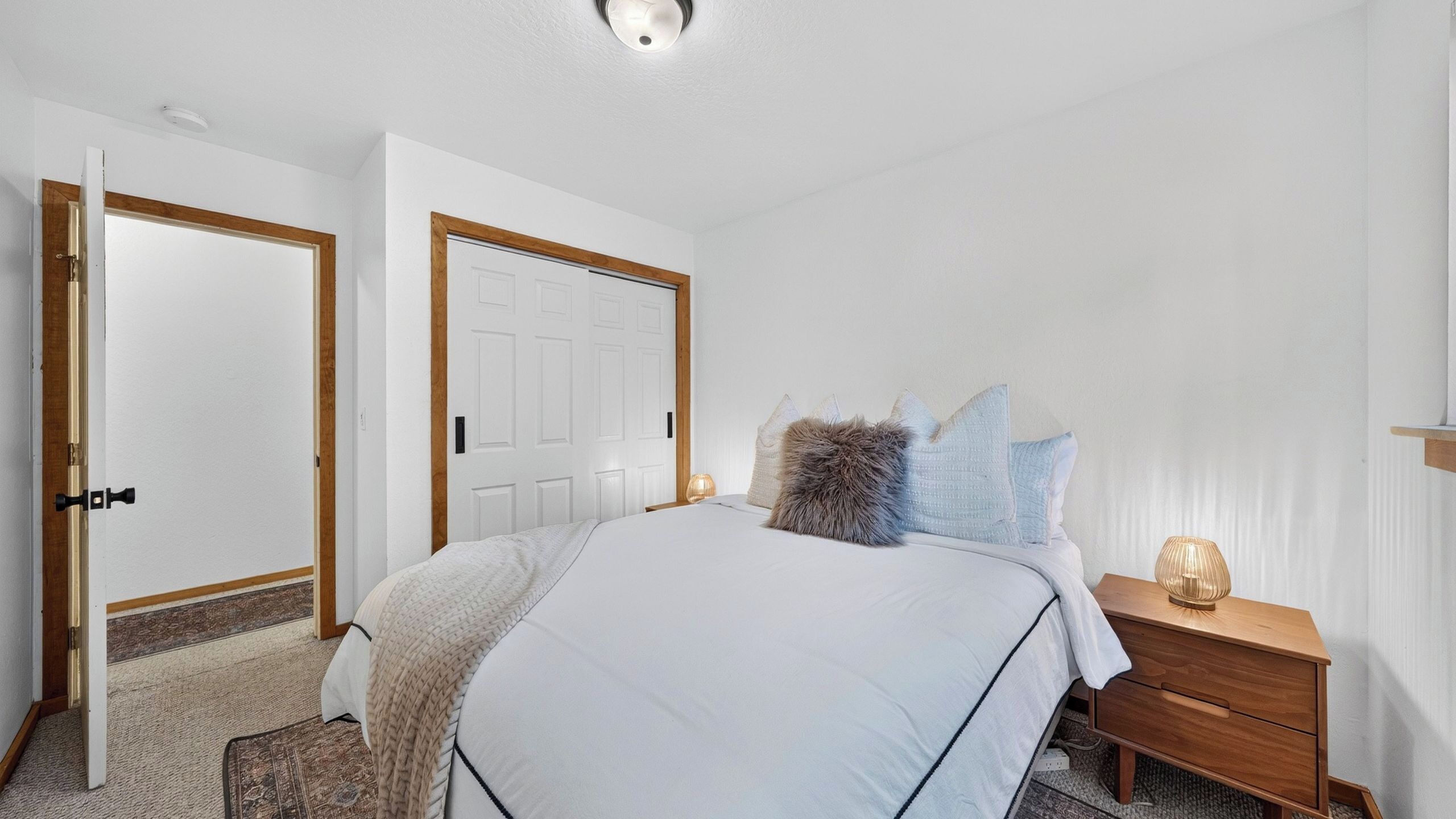 Een slaapkamer met een bed, nachtkastje, lamp en een deur.