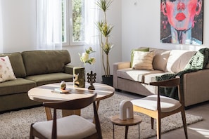 A living room with a sofa, chairs, a coffee table, a vase with flowers, a potted plant, and a painting on the wall. - Villa Madero 10 Apartment (Torrent)