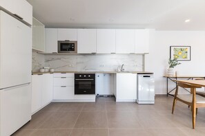 A modern kitchen with white cabinetry, a built-in oven, a microwave, and a refrigerator.