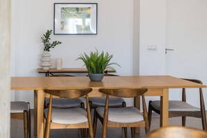 A dining area with a wooden table, six chairs, a potted fern, a framed picture on the wall, and a small plant on the side table. - Villa Madero 10 Apartment (Torrent)