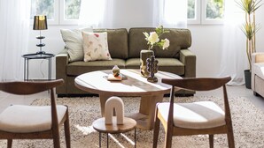 Una sala de estar con sofá, dos sillones, una mesa de centro, una lámpara y un florero con flores.
