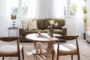 A living room with a sofa, two chairs, a coffee table, a lamp, and a vase with flowers.